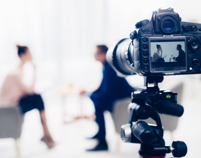 businessman giving interview to journalist in office, camera on tripod on foreground