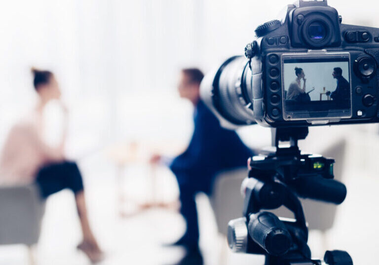 businessman giving interview to journalist in office, camera on tripod on foreground